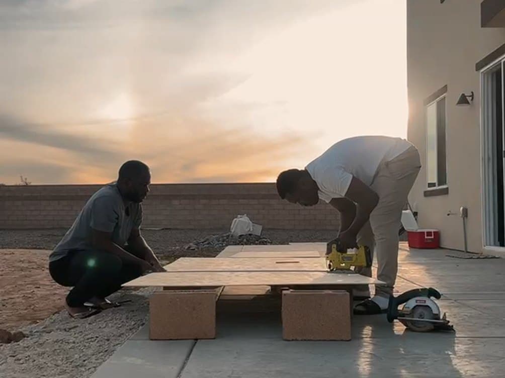 Two Genix crew members cutting panels on a patio at sunset